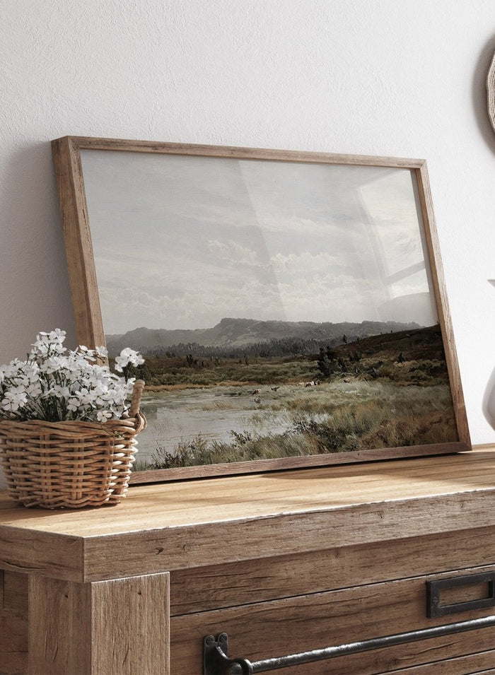 A framed landscape art print depicting a muted, overcast valley scene with a small body of water, grassy foreground, distant hills, and a cloudy sky, shown against a light neutral background. A View of Fleet Moor, Surrey by Alfred de Bréanski is a vintage English landscape print featuring cattle, water, rolling hills, open countryside, and a cloudy sky.