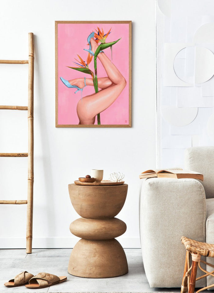 Legs wearing blue high heels with a pink background and bird of paradise flower. Bird of Paradise by Alexander Grahovsky art print featuring crossed legs in blue heels and a bold tropical flower on a pink background. Officially licensed surreal wall poster.