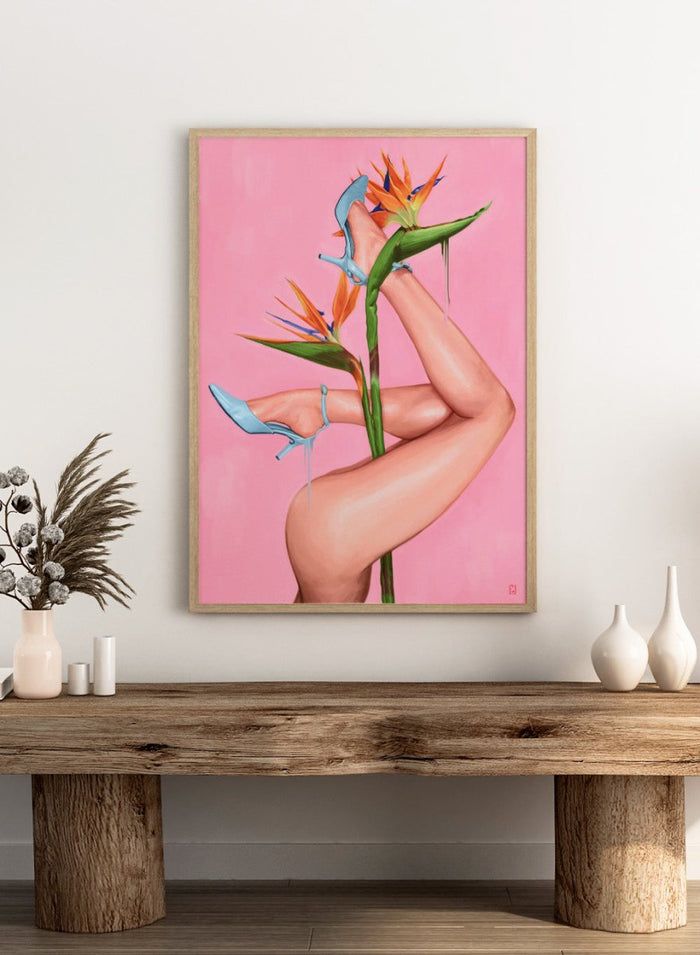 Legs wearing blue high heels with a pink background and bird of paradise flower. Bird of Paradise by Alexander Grahovsky art print featuring crossed legs in blue heels and a bold tropical flower on a pink background. Officially licensed surreal wall poster.