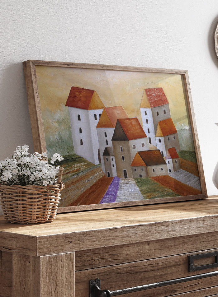 A framed landscape painting depicting stylized white buildings with orange-brown roofs, set in a field with a purple path under a warm yellow sky. Shop Peaceful Lavender Village by Angeles M. Pomata, an autumn village landscape art print featuring white houses, terracotta roofs, lavender fields, and warm earthy tones.