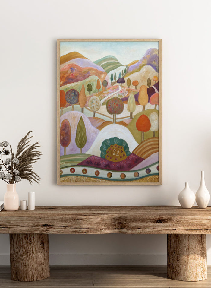 A colorful landscape painting featuring stylized hills, rolling hills, and trees in pastel and earthy tones. Shop Whimsical Autumn Landscape by Angeles M. Pomata, a colorful fall landscape art print featuring rolling hills, winding paths, and stylized autumn trees.