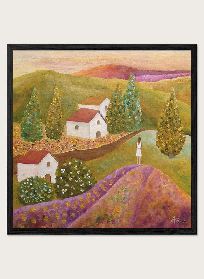 A framed landscape painting featuring rolling green hills, white houses with red roofs, tall conical trees, and a figure standing on a purple field. Shop Woman in Lavender Fields by Angeles M. Pomata, a colorful landscape and figurative art print featuring lavender fields, white houses, cypress trees, and rolling hills.