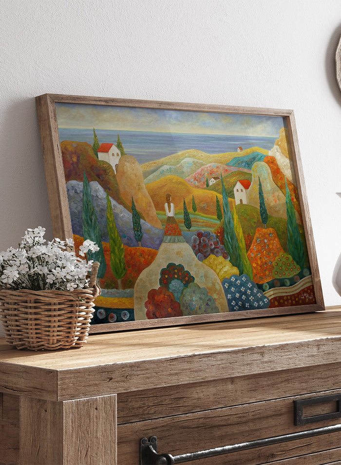 A framed landscape painting featuring stylized hills, cypress trees, small houses with red roofs, and a blue sea under a pale sky. Shop Woman in Mediterranean Landscape by Angeles M. Pomata, a colorful Mediterranean landscape and figurative art print with cypress trees, white houses, hills, and sea views.