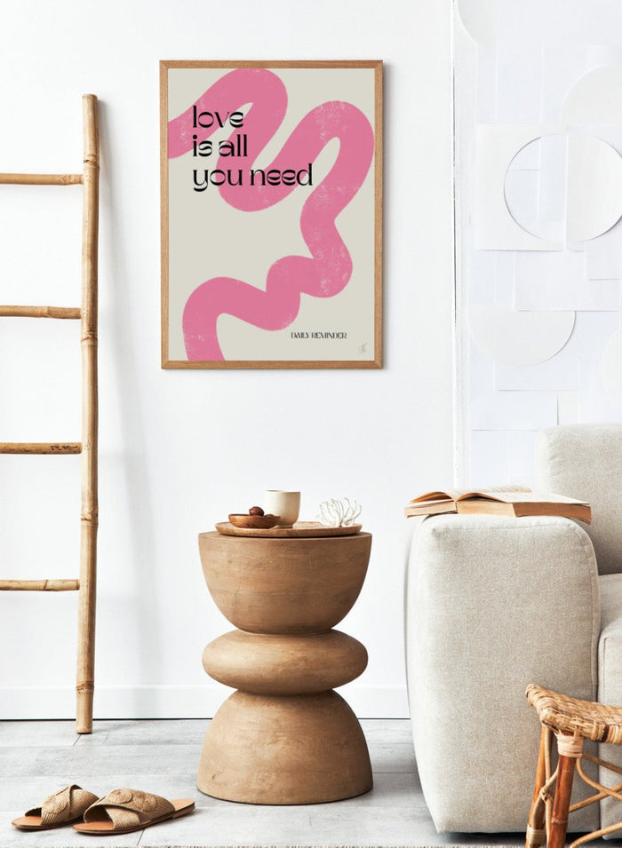Poster with pink abstract design and 'love is all you need' text on a light background. Love Is All You Need by Anne-Marie Volfova is a typography art print with bold lettering and pink abstract brushstrokes. A modern love wall poster.