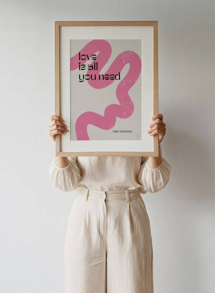 Poster with pink abstract design and 'love is all you need' text on a light background. Love Is All You Need by Anne-Marie Volfova is a typography art print with bold lettering and pink abstract brushstrokes. A modern love wall poster.