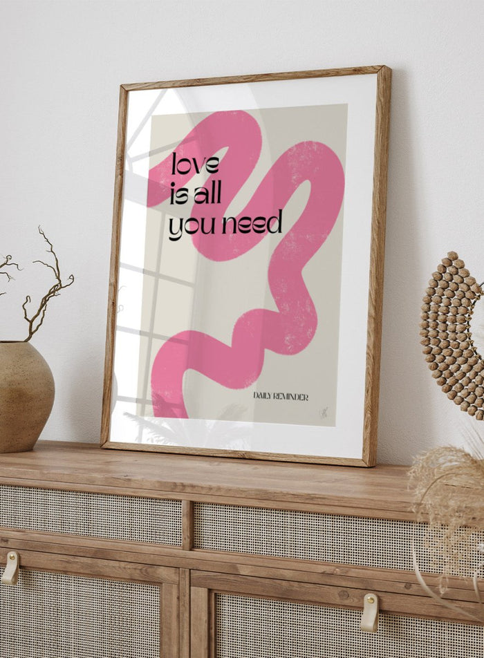 Poster with pink abstract design and 'love is all you need' text on a light background. Love Is All You Need by Anne-Marie Volfova is a typography art print with bold lettering and pink abstract brushstrokes. A modern love wall poster.