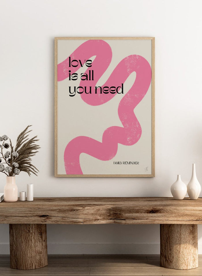 Poster with pink abstract design and 'love is all you need' text on a light background. Love Is All You Need by Anne-Marie Volfova is a typography art print with bold lettering and pink abstract brushstrokes. A modern love wall poster.