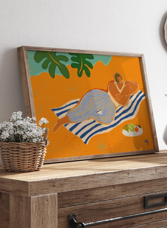 Framed artwork of a woman lounging on a towel with a plate of fruit against an orange background. A Day at the Beach by Arty Guava is a colorful coastal art print featuring a relaxed beach scene, tropical foliage, bold color, and contemporary illustration.