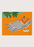 Framed artwork of a woman lounging on a towel with a plate of fruit against an orange background. A Day at the Beach by Arty Guava is a colorful coastal art print featuring a relaxed beach scene, tropical foliage, bold color, and contemporary illustration.