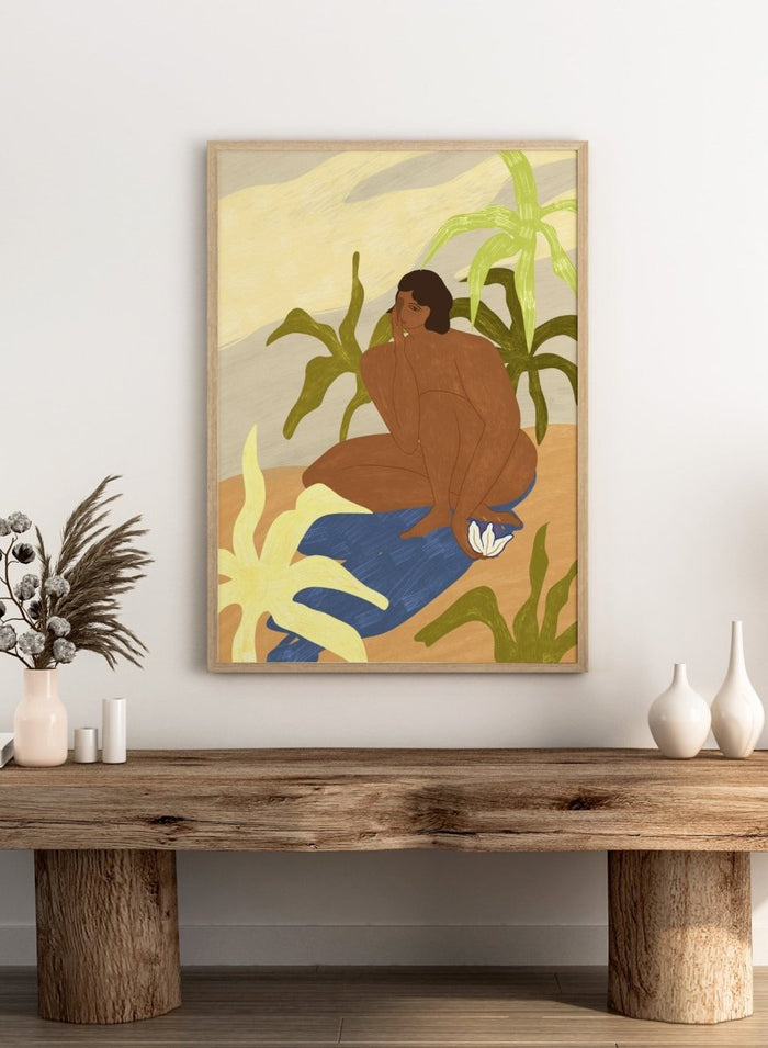 An art print featuring a stylized illustration of a seated figure with dark hair, surrounded by green tropical leaves, a blue cloth, and a white flower, set against a sandy beige and cream background. Au Naturel by Arty Guava premium framed fine art print featuring a seated woman surrounded by oversized tropical plants in warm earthy tones.