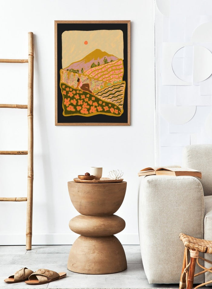 Illustration of a person sitting on a hill with a mountain and sunset in the background. Field Of Flowers by Arty Guava is a colorful landscape art print featuring blooming fields, rolling hills, nature-inspired illustration, and contemporary wall art.