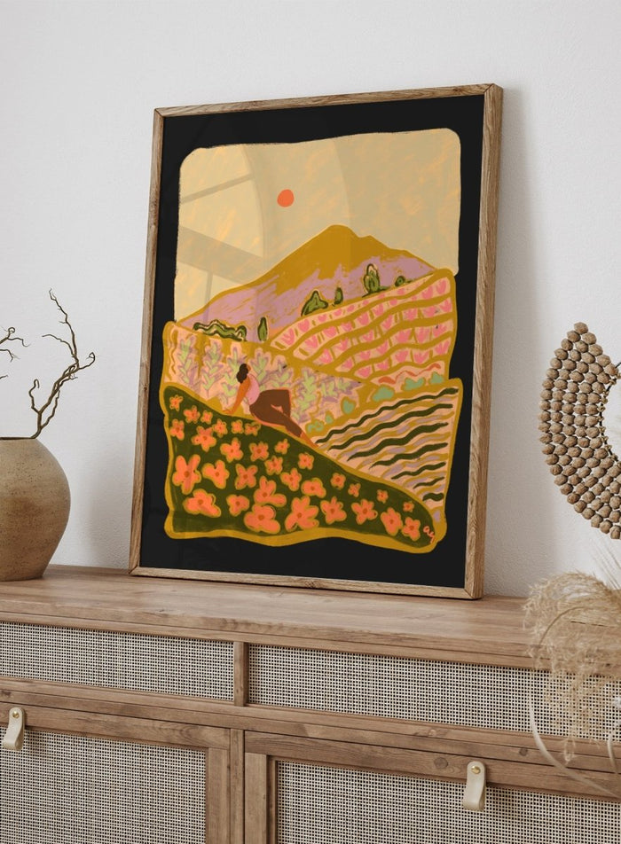 Illustration of a person sitting on a hill with a mountain and sunset in the background. Field Of Flowers by Arty Guava is a colorful landscape art print featuring blooming fields, rolling hills, nature-inspired illustration, and contemporary wall art.