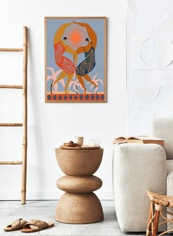 Artistic depiction of two dancers with a sun in the center on a blue background. Sisterhood by Arty Guava is a modern art print of two women dancing under the sun, celebrating friendship and unity. Officially licensed wall poster.