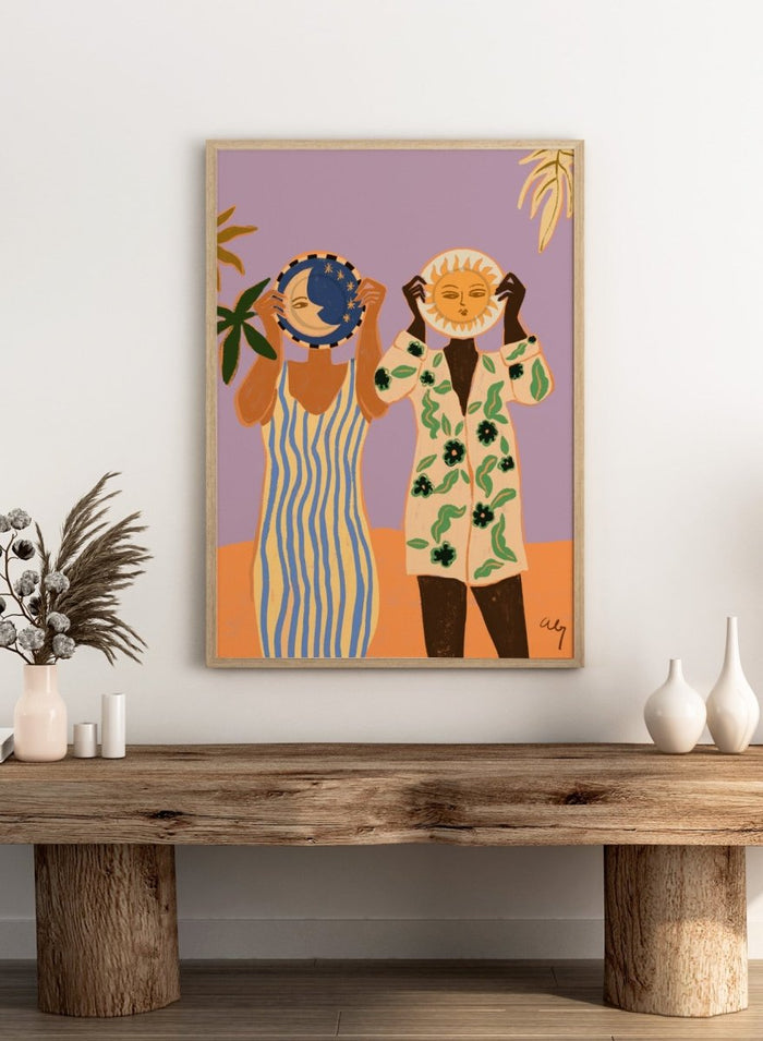 Two people holding celestial objects against a purple background. Sun and Moon by Arty Guava is a playful contemporary art print featuring female figures, celestial motifs, bold color, tropical influences, and modern illustration.