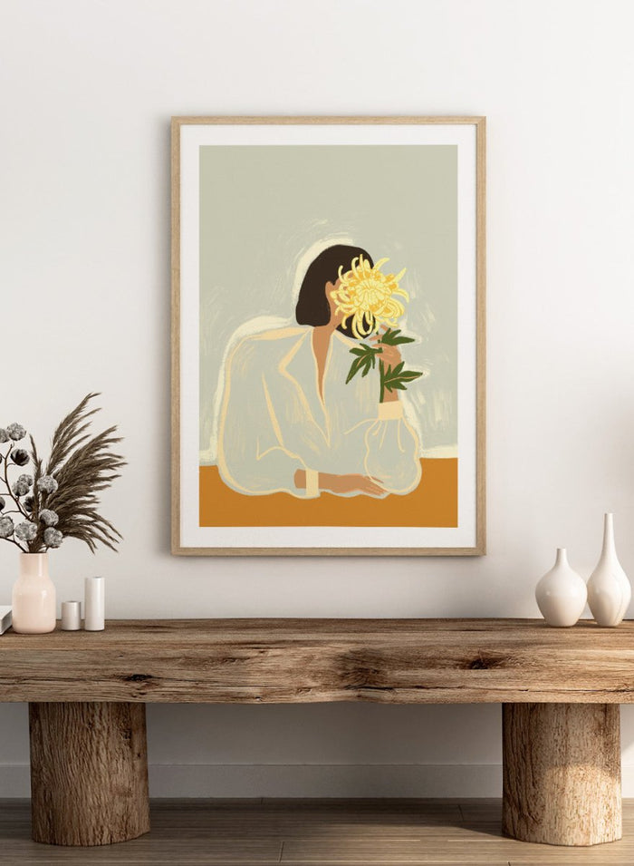 Illustration of a woman in a white dress holding a large yellow flower against a light background. The Chrysanthemum by Arty Guava is a modern portrait illustration featuring a woman with flowers, contemporary floral wall art style, and officially licensed artwork.