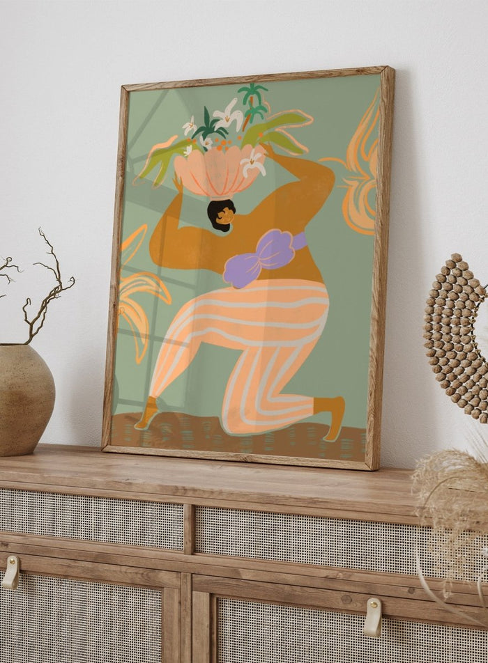 A stylized art print featuring a woman in flowing peach and white striped pants with a purple sash, carrying a large flower basket on her head against a muted sage green background. The Weight of the World by Arty Guava premium framed fine art print featuring a woman carrying tropical flowers in soft green, peach, and lilac tones.
