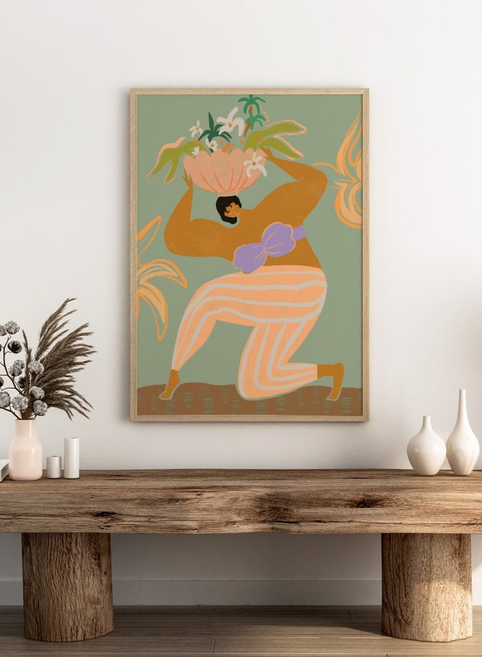 A stylized art print featuring a woman in flowing peach and white striped pants with a purple sash, carrying a large flower basket on her head against a muted sage green background. The Weight of the World by Arty Guava premium framed fine art print featuring a woman carrying tropical flowers in soft green, peach, and lilac tones.