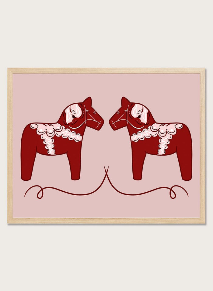 Two red Dala horse figures with white patterns on a pink background. Nordic Horses Twins by Athene Fritsch is a Scandinavian folk art illustration art print featuring Swedish Dala horses, bold red color, and modern wall art design.