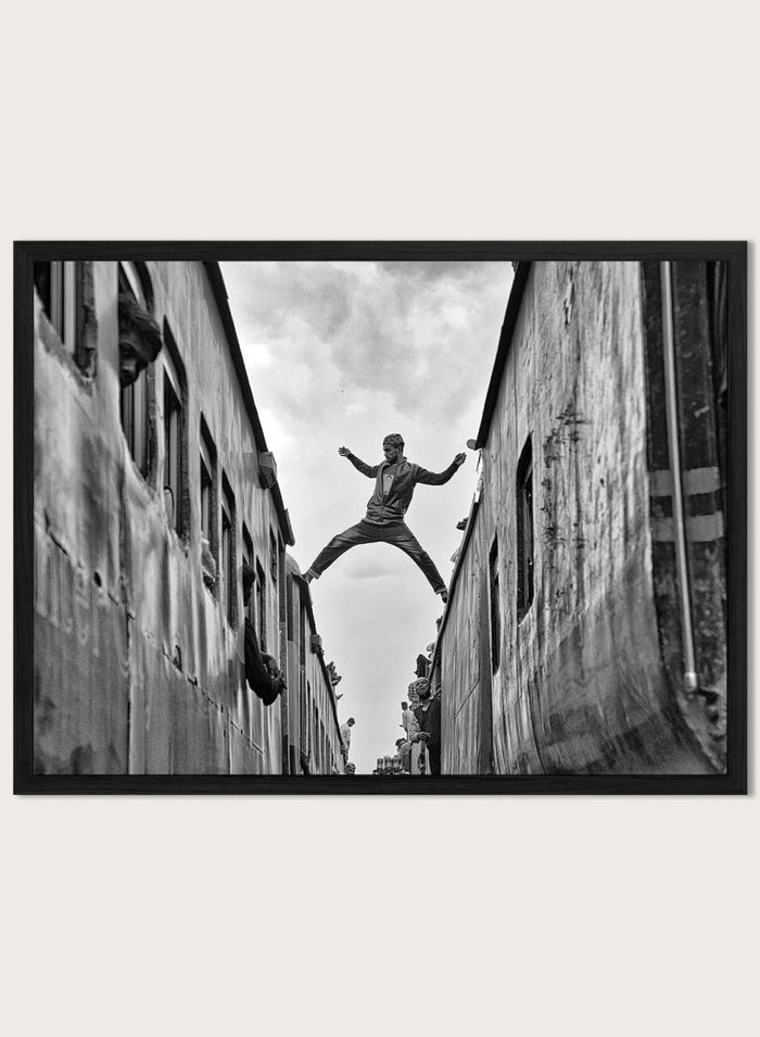 Superman by Azim Khan Ronnie black and white photography print of man jumping between trains in Bangladesh, urban action wall art poster