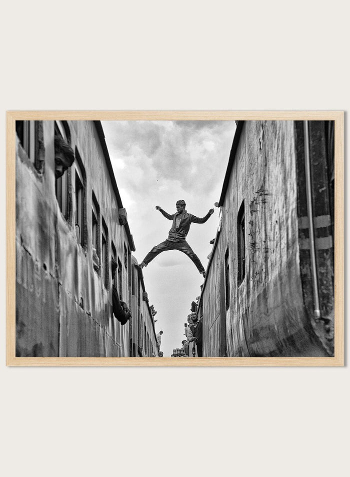 Superman by Azim Khan Ronnie black and white photography print of man jumping between trains in Bangladesh, urban action wall art poster