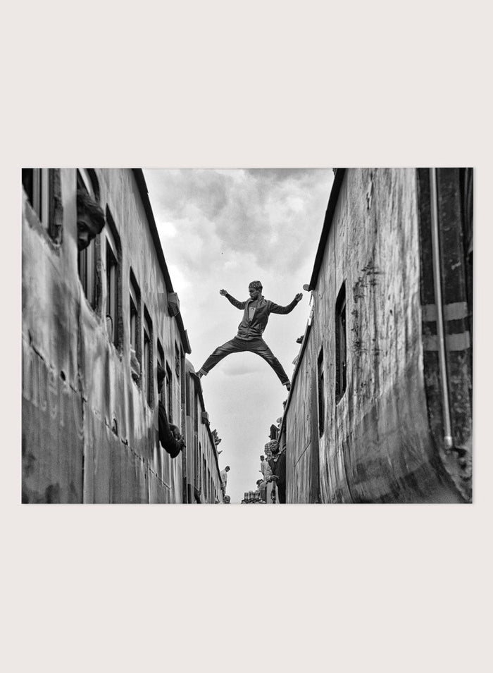 Superman by Azim Khan Ronnie black and white photography print of man jumping between trains in Bangladesh, urban action wall art poster