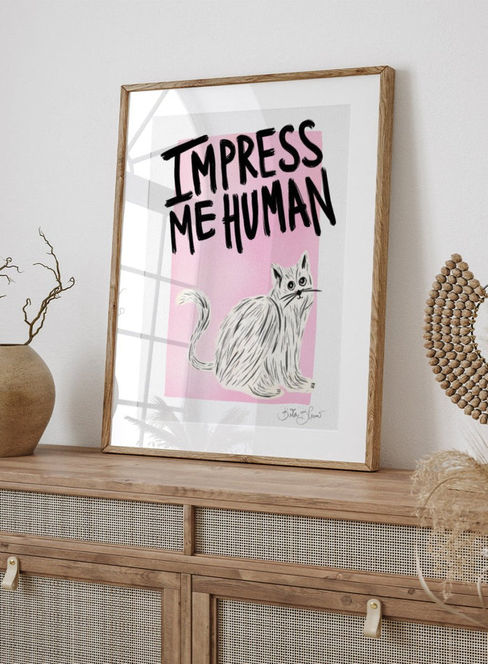 Cartoon cat with 'Impress Me Human' text on a pink background. Cat Owner. Impress Me Human by Baroo Bloom is a playful cat art print featuring hand-drawn illustration and humorous typography. Officially licensed wall poster with optional framing.