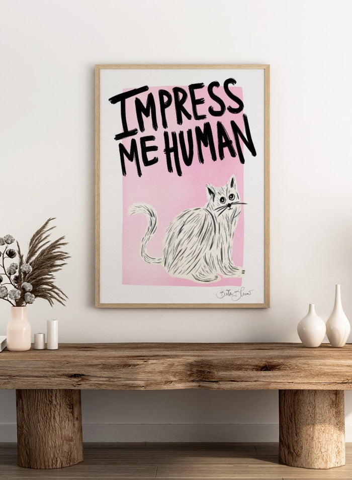 Cartoon cat with 'Impress Me Human' text on a pink background. Cat Owner. Impress Me Human by Baroo Bloom is a playful cat art print featuring hand-drawn illustration and humorous typography. Officially licensed wall poster with optional framing.