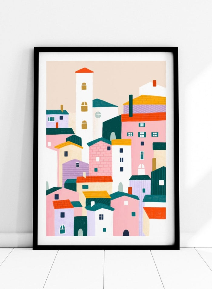 A framed minimalist art print depicting a cluster of stylized pastel houses and a church tower in pink, peach, teal, yellow, and cream tones. Charming Colorful Houses by Bea Müller premium framed fine art print featuring a playful town of pink, lavender, cream, and teal buildings.