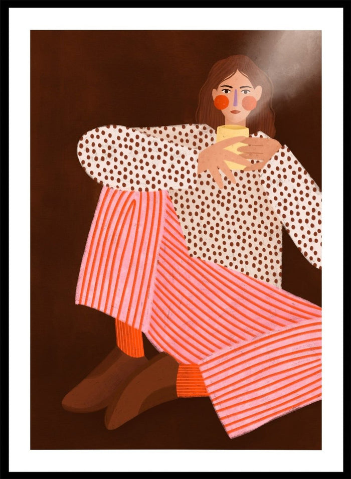 A framed art print featuring a stylized illustration of a woman in a white blouse with brown polka dots and pink-and-white striped trousers, holding a yellow cup against a dark brown background. Cozy Coffee Moment by Bea Müller premium framed fine art print featuring a woman curled up with a warm mug in bold pink, red, and brown tones.