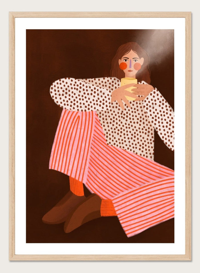 A framed art print featuring a stylized illustration of a woman in a white blouse with brown polka dots and pink-and-white striped trousers, holding a yellow cup against a dark brown background. Cozy Coffee Moment by Bea Müller premium framed fine art print featuring a woman curled up with a warm mug in bold pink, red, and brown tones.