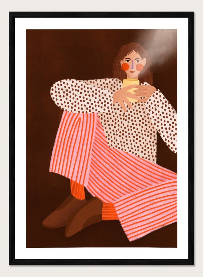 A framed art print featuring a stylized illustration of a woman in a white blouse with brown polka dots and pink-and-white striped trousers, holding a yellow cup against a dark brown background. Cozy Coffee Moment by Bea Müller premium framed fine art print featuring a woman curled up with a warm mug in bold pink, red, and brown tones.