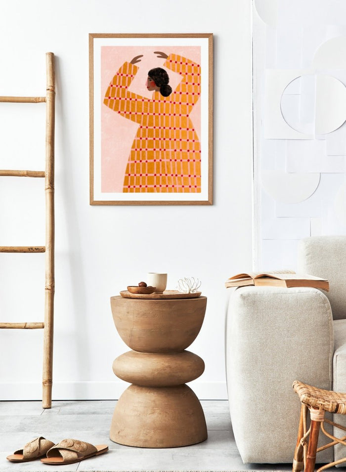 A framed art print featuring a stylized illustration of a woman in profile wearing a bright orange dress with a red grid pattern, set against a pale pink background. Dancing Woman in Orange by Bea Müller premium fine art print featuring a bold figure, warm orange tones, and a playful graphic composition.