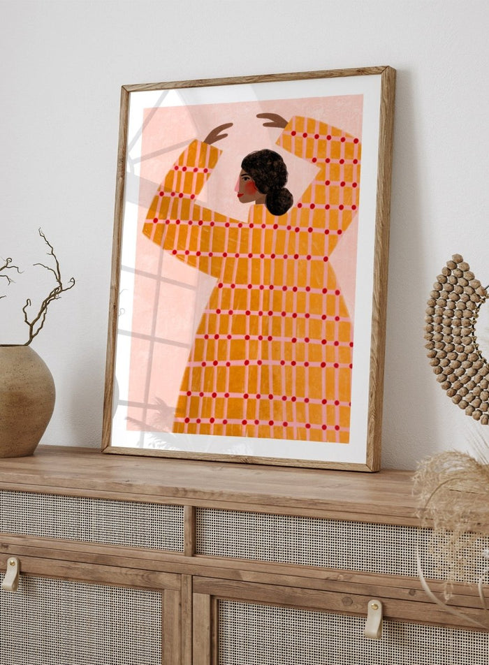 A framed art print featuring a stylized illustration of a woman in profile wearing a bright orange dress with a red grid pattern, set against a pale pink background. Dancing Woman in Orange by Bea Müller premium fine art print featuring a bold figure, warm orange tones, and a playful graphic composition.