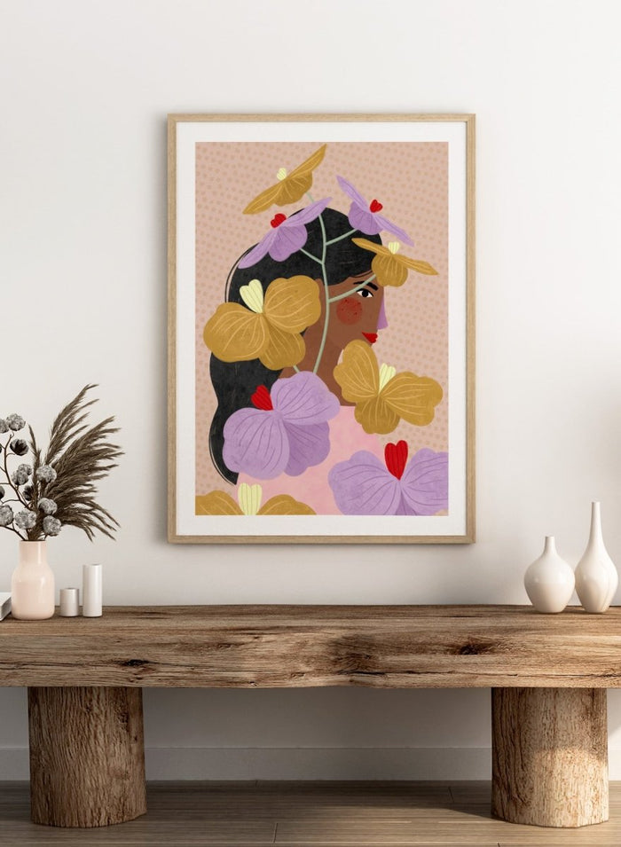 A framed art print featuring a stylized illustration of a woman with dark hair surrounded by large purple and yellow flowers on a beige patterned background. Floral Woman Portrait by Bea Müller premium framed fine art print featuring a woman surrounded by oversized lilac, mustard, and red flowers.