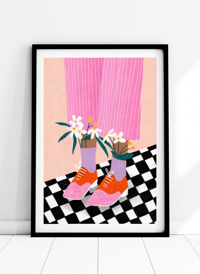 A stylized fashion illustration of a person's legs wearing pink pinstripe trousers, lavender socks, orange and pink shoes, and holding white flowers, set against a peach background with a black-and-white checkered floor. Flowering Oxford Style by Bea Müller premium framed fine art print featuring colorful Oxford shoes, lilac socks, and flowers on a checkered floor.