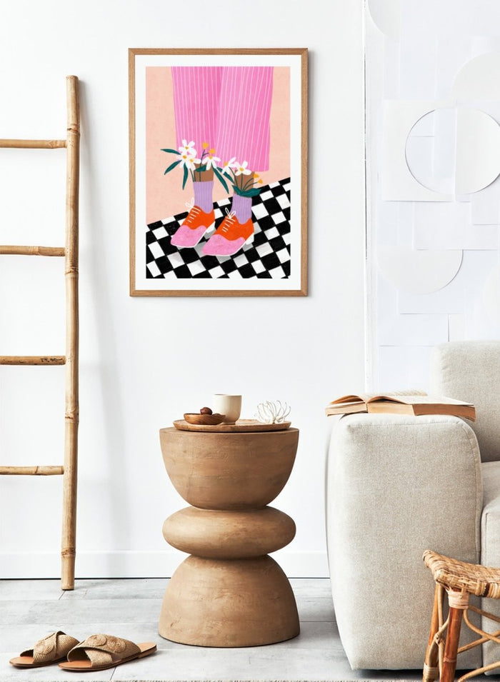A stylized fashion illustration of a person's legs wearing pink pinstripe trousers, lavender socks, orange and pink shoes, and holding white flowers, set against a peach background with a black-and-white checkered floor. Flowering Oxford Style by Bea Müller premium framed fine art print featuring colorful Oxford shoes, lilac socks, and flowers on a checkered floor.
