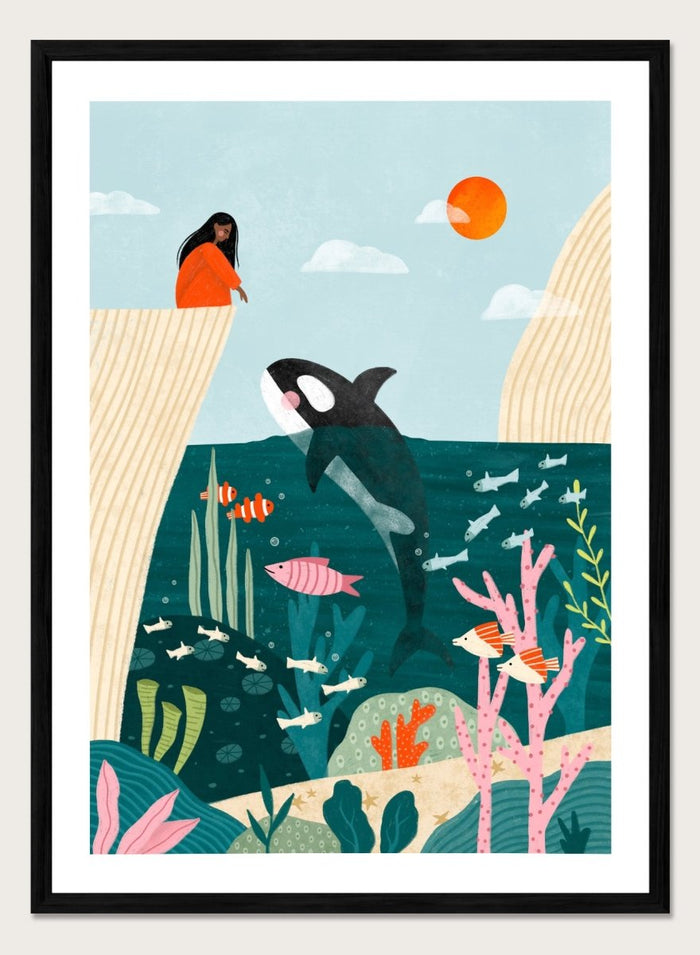 A framed art print featuring a whimsical underwater scene with an orca, coral, fish, and a woman in an orange dress standing on a cliff edge under a sun. Girl Watches Ocean Life by Bea Müller premium framed fine art print featuring a child watching an orca swim through a colorful underwater world.