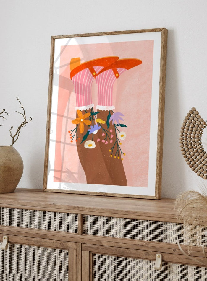 A stylized art print featuring a pair of legs wearing pink striped socks with white ruffles, decorated with colorful wildflowers, and topped with orange high-heeled shoes, set against a textured pink background. Happy Feet and Flowers by Bea Müller premium framed fine art print featuring red Mary Janes, striped socks, and colorful flowers on a soft pink background.
