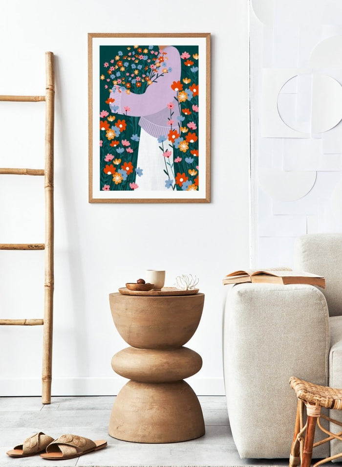 A stylized art print featuring a woman in a lavender sweater and white skirt holding a large bouquet of colorful wildflowers, framed by dense flowers on a dark teal background. Happy Woman Holding Flowers by Bea Müller premium framed fine art print featuring a woman carrying wildflowers in bright orange, pink, blue, and teal.