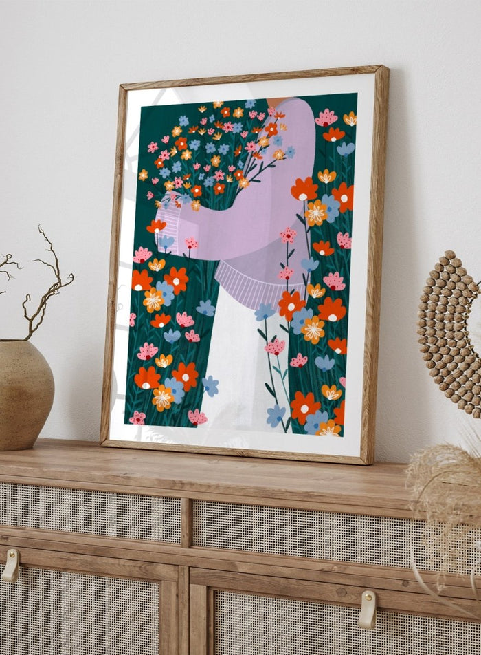 A stylized art print featuring a woman in a lavender sweater and white skirt holding a large bouquet of colorful wildflowers, framed by dense flowers on a dark teal background. Happy Woman Holding Flowers by Bea Müller premium framed fine art print featuring a woman carrying wildflowers in bright orange, pink, blue, and teal.