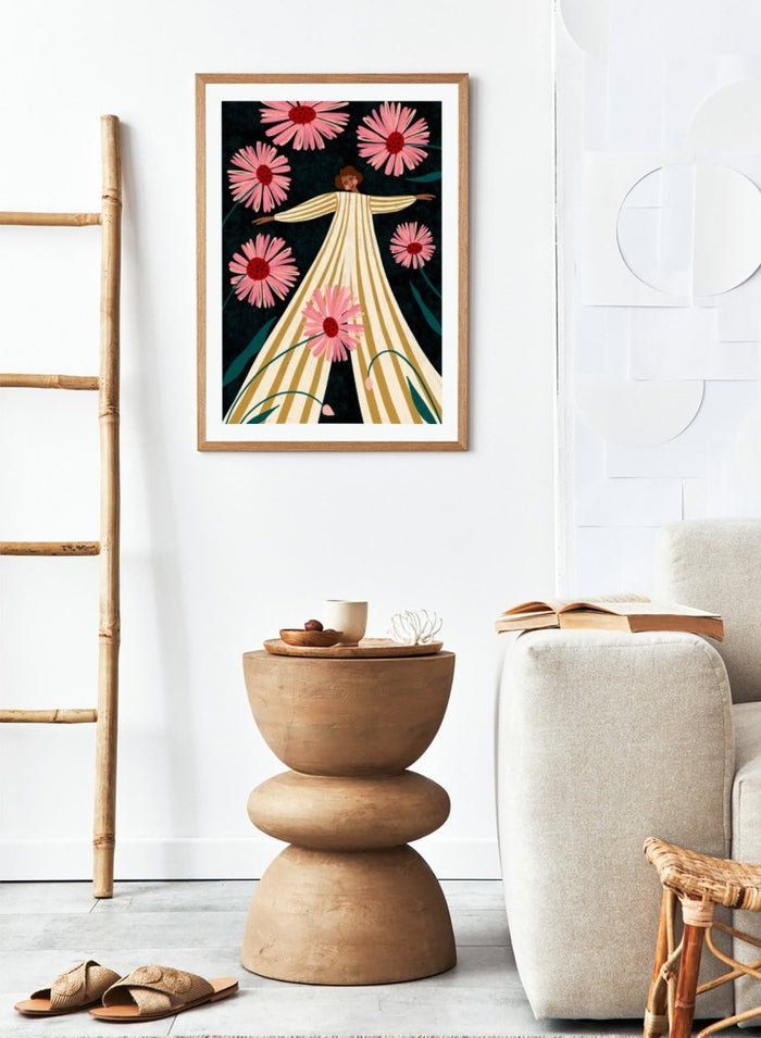 A framed art print featuring a stylized illustration of a woman in a cream and gold striped dress surrounded by large pink flowers on a dark background. Joyful Woman In Bloom by Bea Müller premium framed fine art print featuring a woman in a striped dress surrounded by oversized pink flowers.