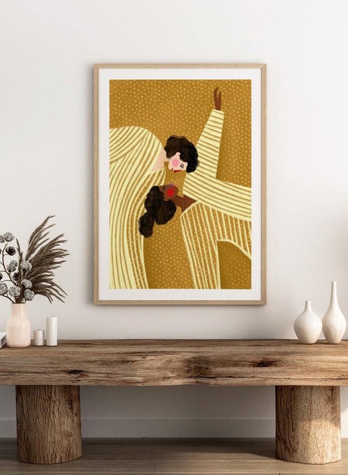 A framed art print featuring a stylized illustration of two women in cream and gold striped dresses against a textured gold background. Loving Embrace by Bea Müller premium fine art print featuring two figures in striped clothing, with warm colors and a bold, intimate composition.