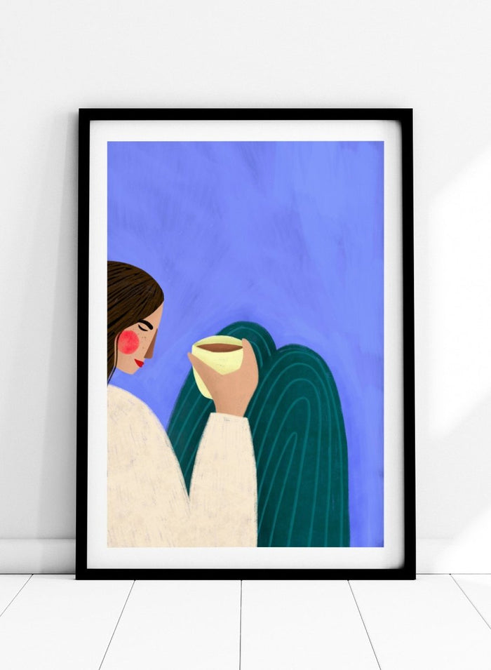 A framed minimalist art print featuring a stylized woman in profile with brown hair, a cream sweater, and a dark teal cape against a textured blue background, holding a pale yellow cup. Peaceful Coffee Moment by Bea Müller premium framed fine art print featuring a woman curled up with a warm drink in soft blue, cream, and teal tones.