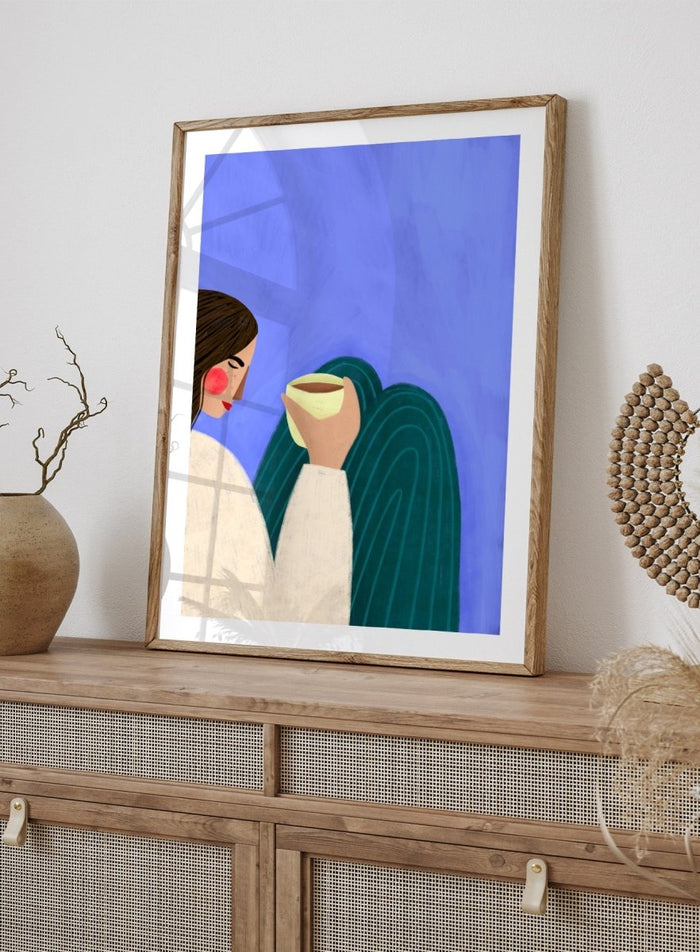 A framed minimalist art print featuring a stylized woman in profile with brown hair, a cream sweater, and a dark teal cape against a textured blue background, holding a pale yellow cup. Peaceful Coffee Moment by Bea Müller premium framed fine art print featuring a woman curled up with a warm drink in soft blue, cream, and teal tones.