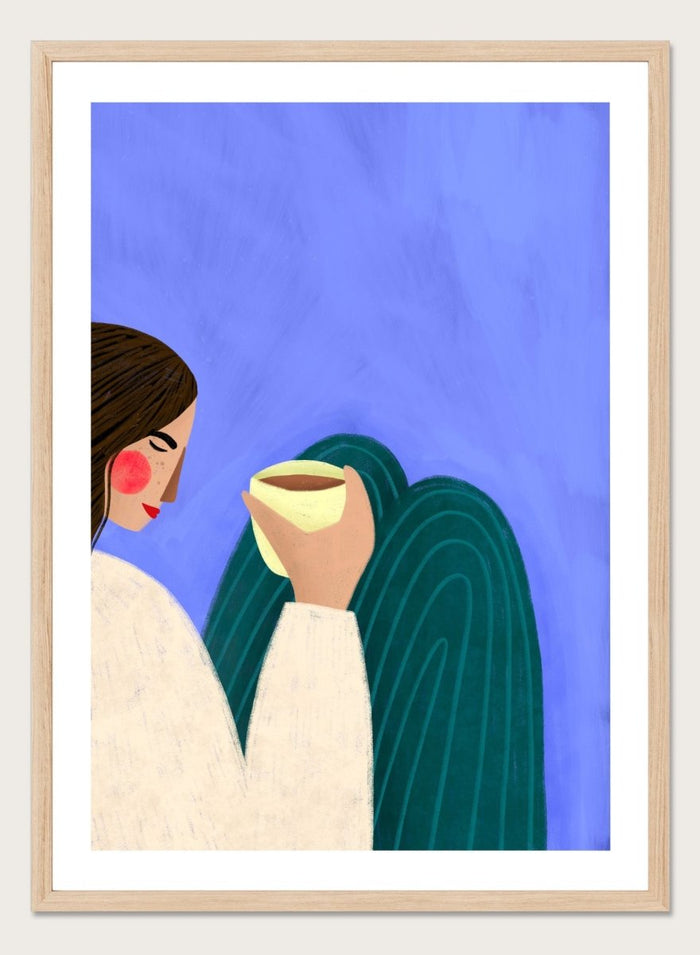 A framed minimalist art print featuring a stylized woman in profile with brown hair, a cream sweater, and a dark teal cape against a textured blue background, holding a pale yellow cup. Peaceful Coffee Moment by Bea Müller premium framed fine art print featuring a woman curled up with a warm drink in soft blue, cream, and teal tones.
