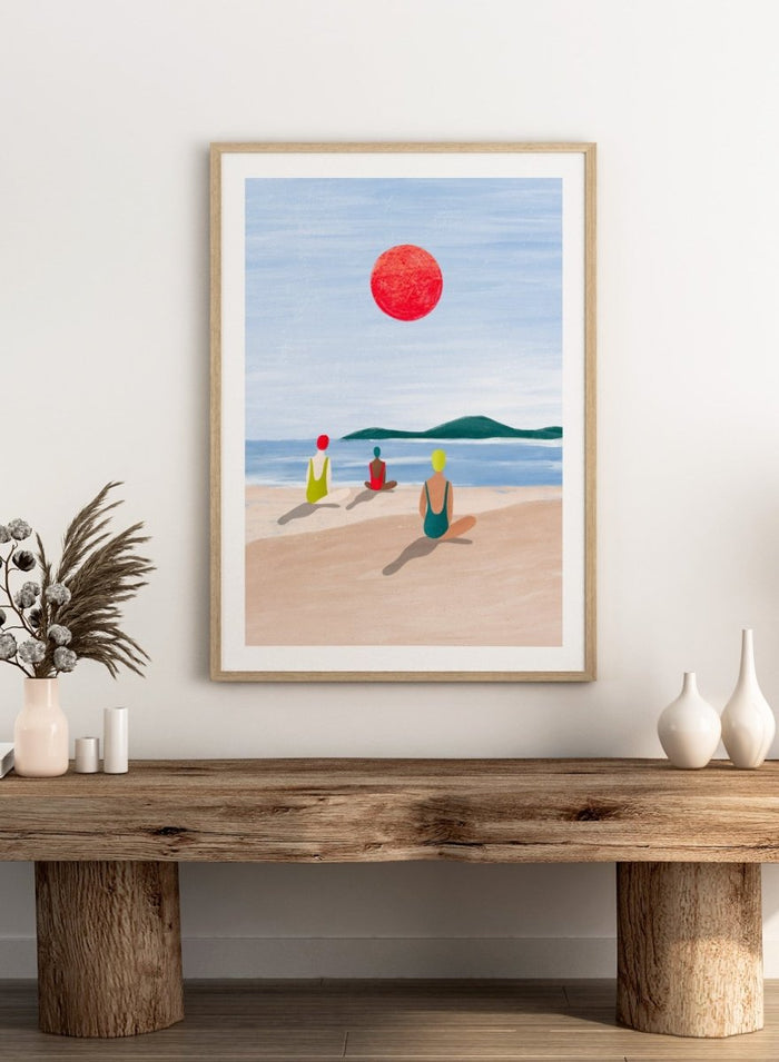 A minimalist art print depicting three figures meditating on a sandy beach under a large red sun. Red Sun Beach Serenity by Bea Müller premium fine art print featuring three figures on a beach beneath a bold red sun in a calm coastal setting.