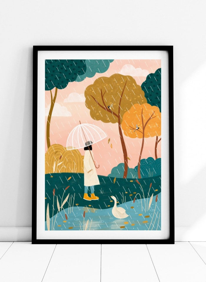A framed art print featuring a whimsical illustration of a person holding a clear umbrella in the rain near a pond with a white goose, surrounded by stylized trees in teal, mustard, and orange tones. Walking In Autumn Rain by Bea Müller premium framed fine art print featuring a woman with an umbrella beside a pond in a colorful rainy landscape.