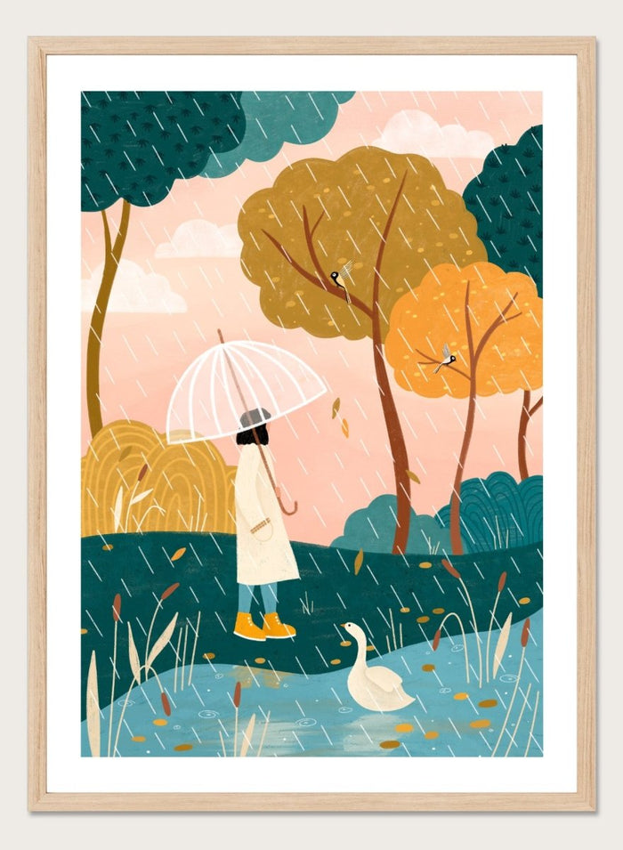 A framed art print featuring a whimsical illustration of a person holding a clear umbrella in the rain near a pond with a white goose, surrounded by stylized trees in teal, mustard, and orange tones. Walking In Autumn Rain by Bea Müller premium framed fine art print featuring a woman with an umbrella beside a pond in a colorful rainy landscape.