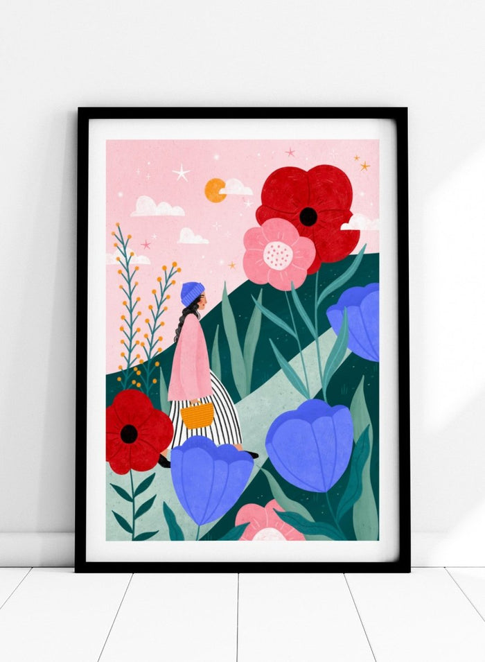 A framed art print featuring a whimsical, colorful illustration of a woman walking through a field of oversized flowers under a pink sky with moon. Whimsical Flower Path by Bea Müller premium fine art print featuring a woman walking among oversized flowers in a bright, playful landscape.