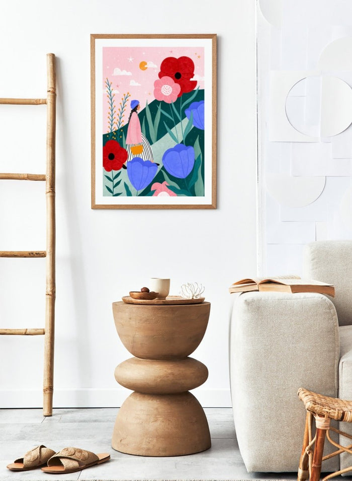 A framed art print featuring a whimsical, colorful illustration of a woman walking through a field of oversized flowers under a pink sky with moon. Whimsical Flower Path by Bea Müller premium fine art print featuring a woman walking among oversized flowers in a bright, playful landscape.